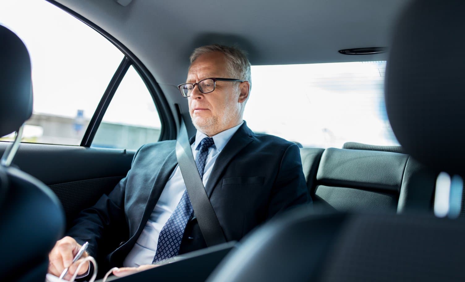 An executive reviewing papers in the back seat of a chauffeured car