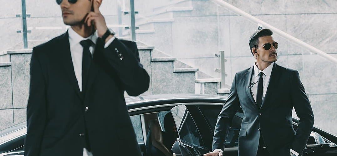 A uniformed chauffeur holding open the door of a black executive van