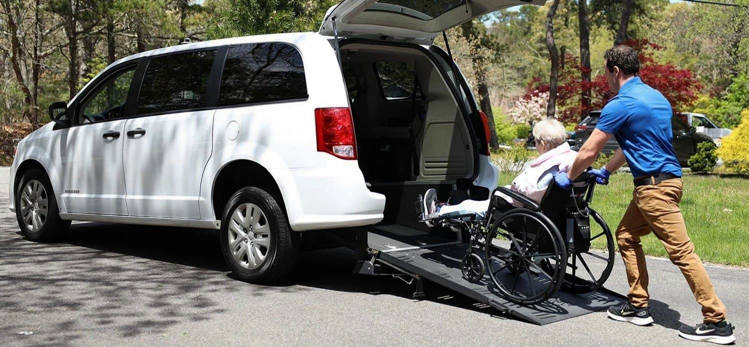 A chauffeur holding open the door of a black sedan for a passenger outside a medical campus
