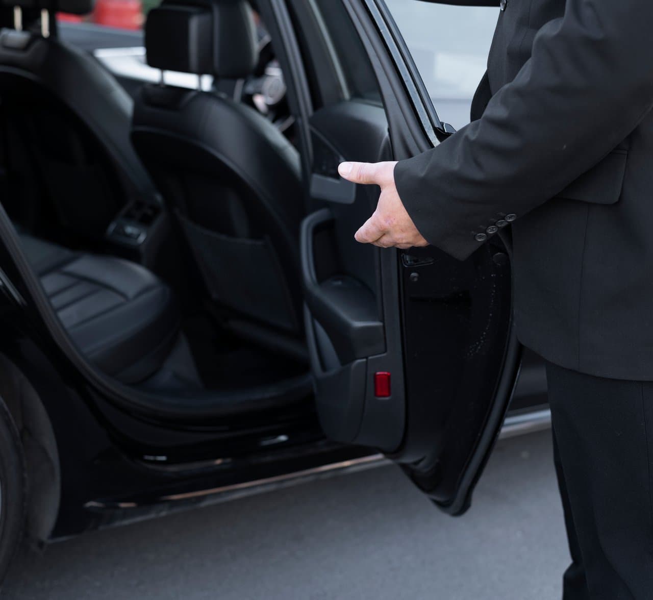 A chauffeur opening the rear door of a black car for a passenger